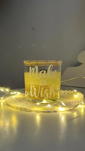 Vela em copo com a gravação Make a Wish, sobre base de luzes